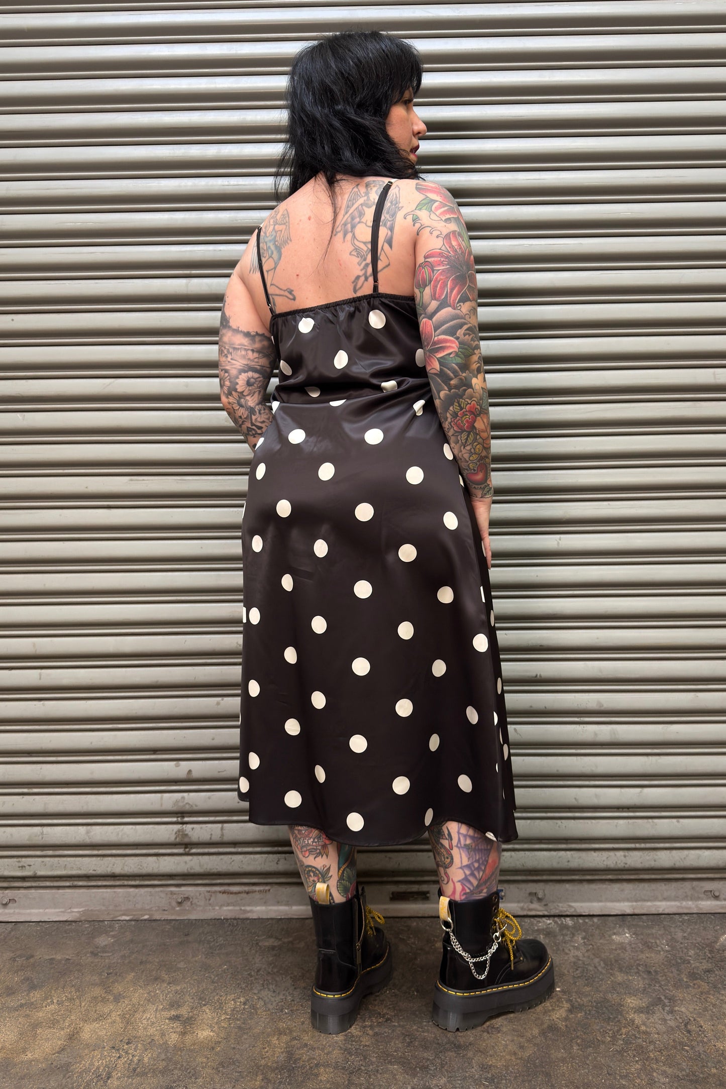 Person wearing a black polka dot dress standing against a metal shutter.