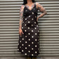 Woman wearing a black dress with white polka dots standing in front of a metal shutter.