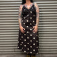 Woman wearing a black dress with white polka dots standing in front of a metal shutter.