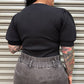Person wearing a black ribbed top and gray pants standing in front of a metallic shutter.