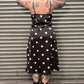 Person wearing a black polka dot dress standing in front of a corrugated metal wall.