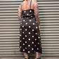 Person wearing a black polka dot dress standing against a metal shutter.