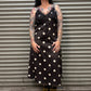 Woman wearing a black dress with white polka dots standing in front of a metal shutter.