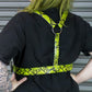 Person wearing a black outfit with a bright yellow and black patterned belt against a metallic background.