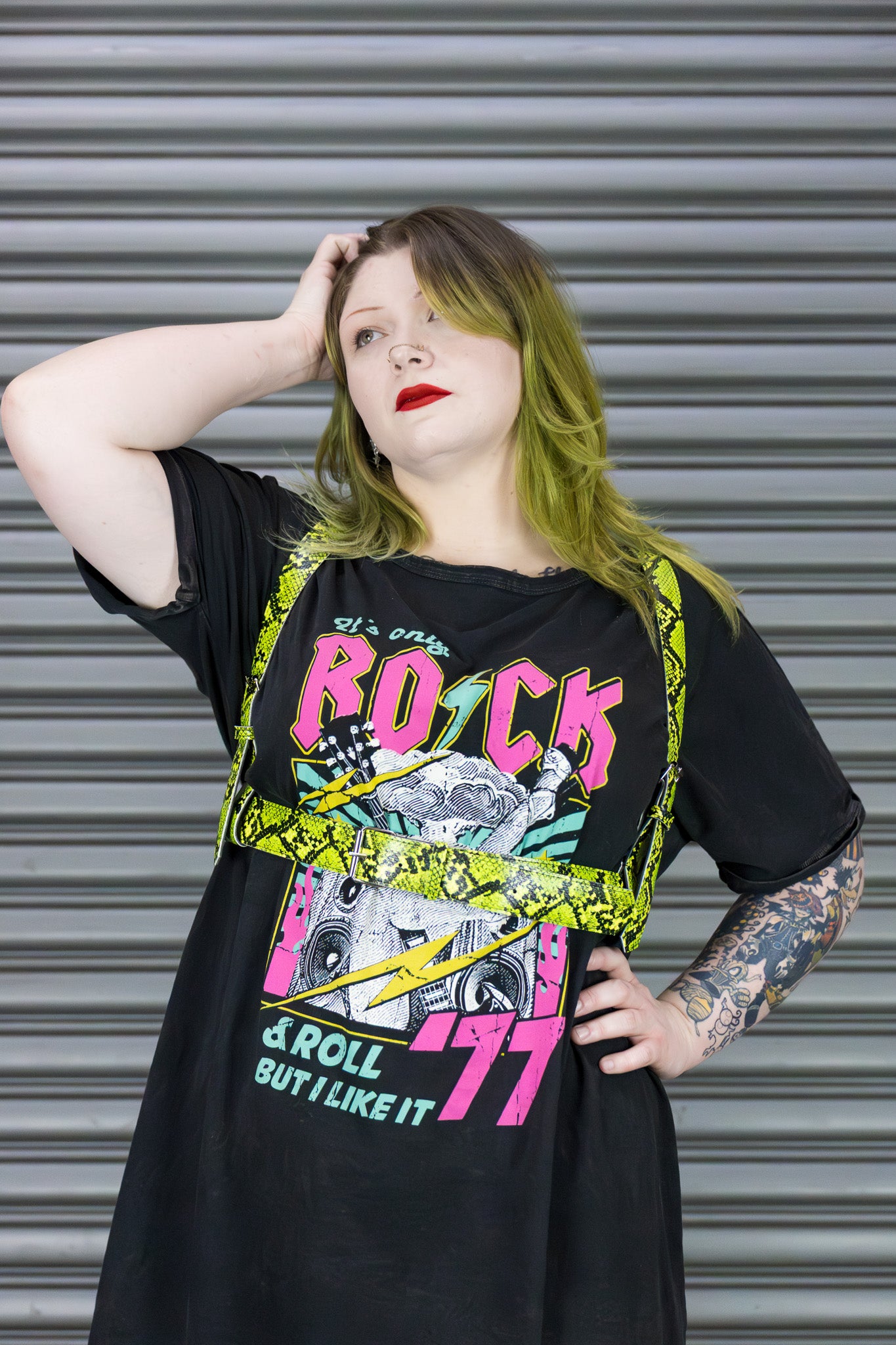 Person wearing a black t-shirt with colorful graphics and text, standing against a metallic shutter.