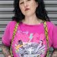 Person wearing a pink t-shirt with rock and roll graphics and yellow suspenders.