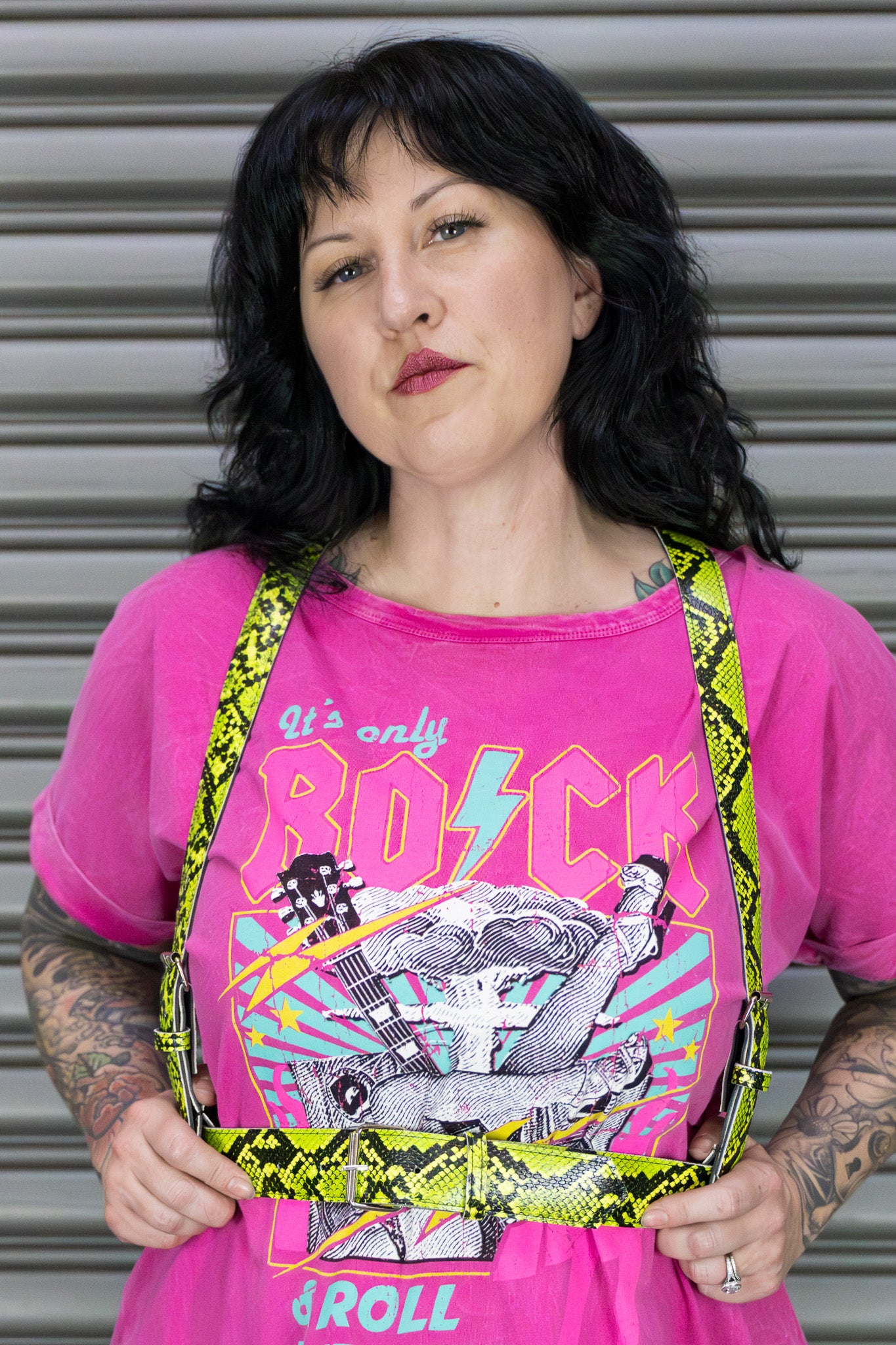 Person wearing a pink t-shirt with rock and roll graphics and yellow suspenders.