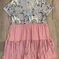 A casual, tiered upcycled tee dress with a mix of patterns, predominantly in pink and other colors, displayed on a wooden floor.