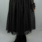 A black midi skirt with a sheer polka-dot overlay and a gathered waist, shown on a model wearing black platform lace-up boots against a light gray background.