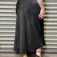 Person wearing a long black skirt standing in front of a metallic shutter.