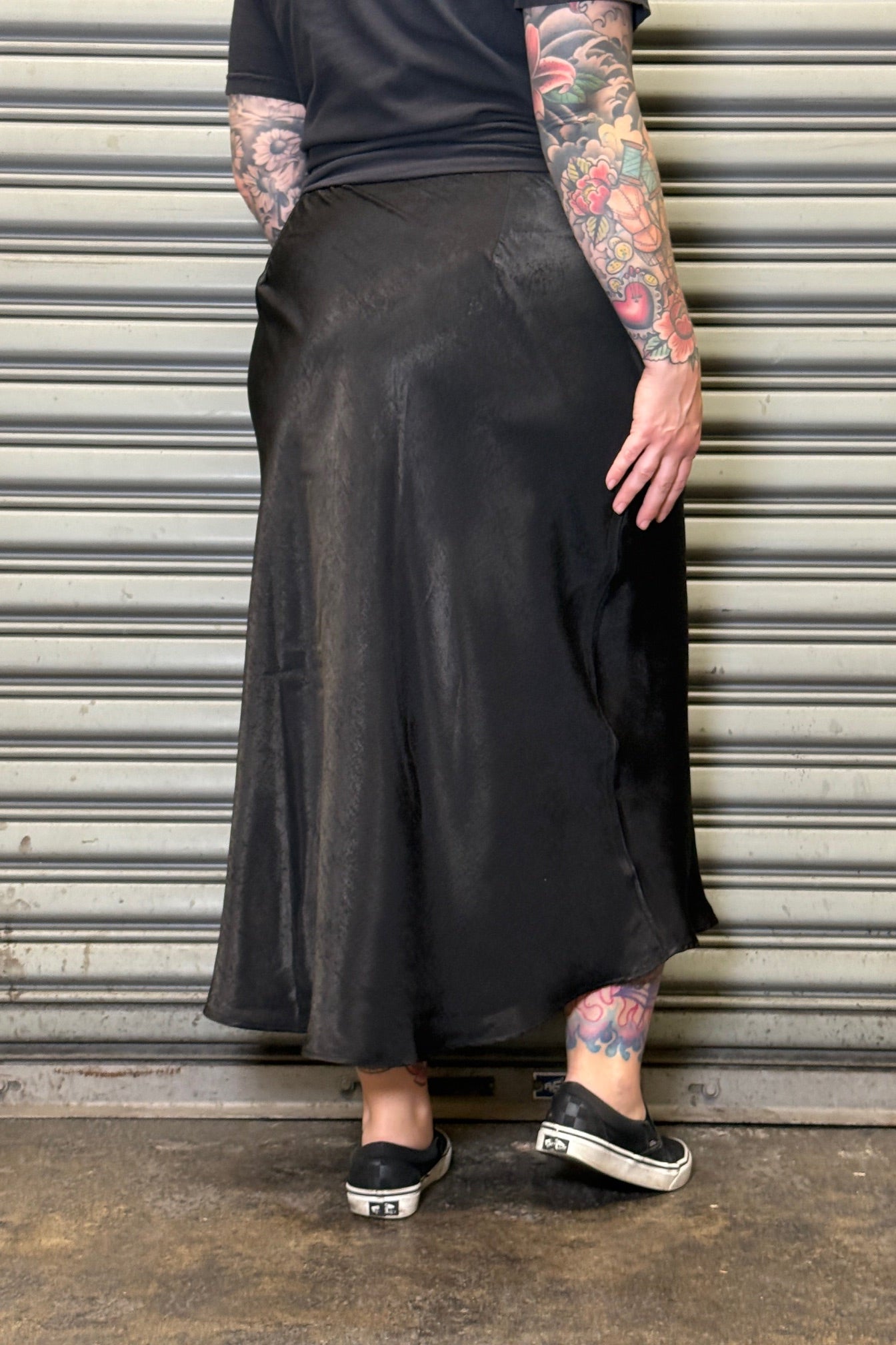 Person wearing a long black skirt standing in front of a metallic shutter.