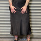 Person wearing a black skirt and black t-shirt with white graphics, standing against a metallic shutter.