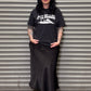 Person wearing a black t-shirt and skirt standing in front of a metal shutter.