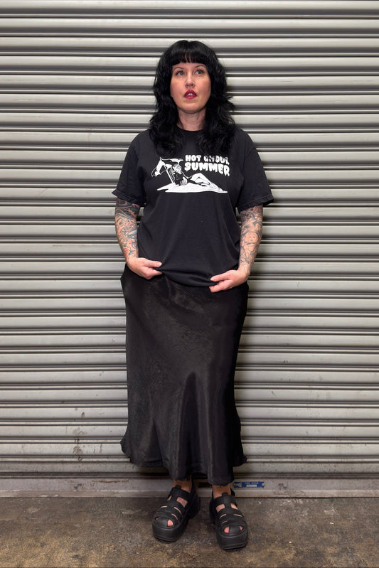Person wearing a black t-shirt and skirt standing in front of a metal shutter.