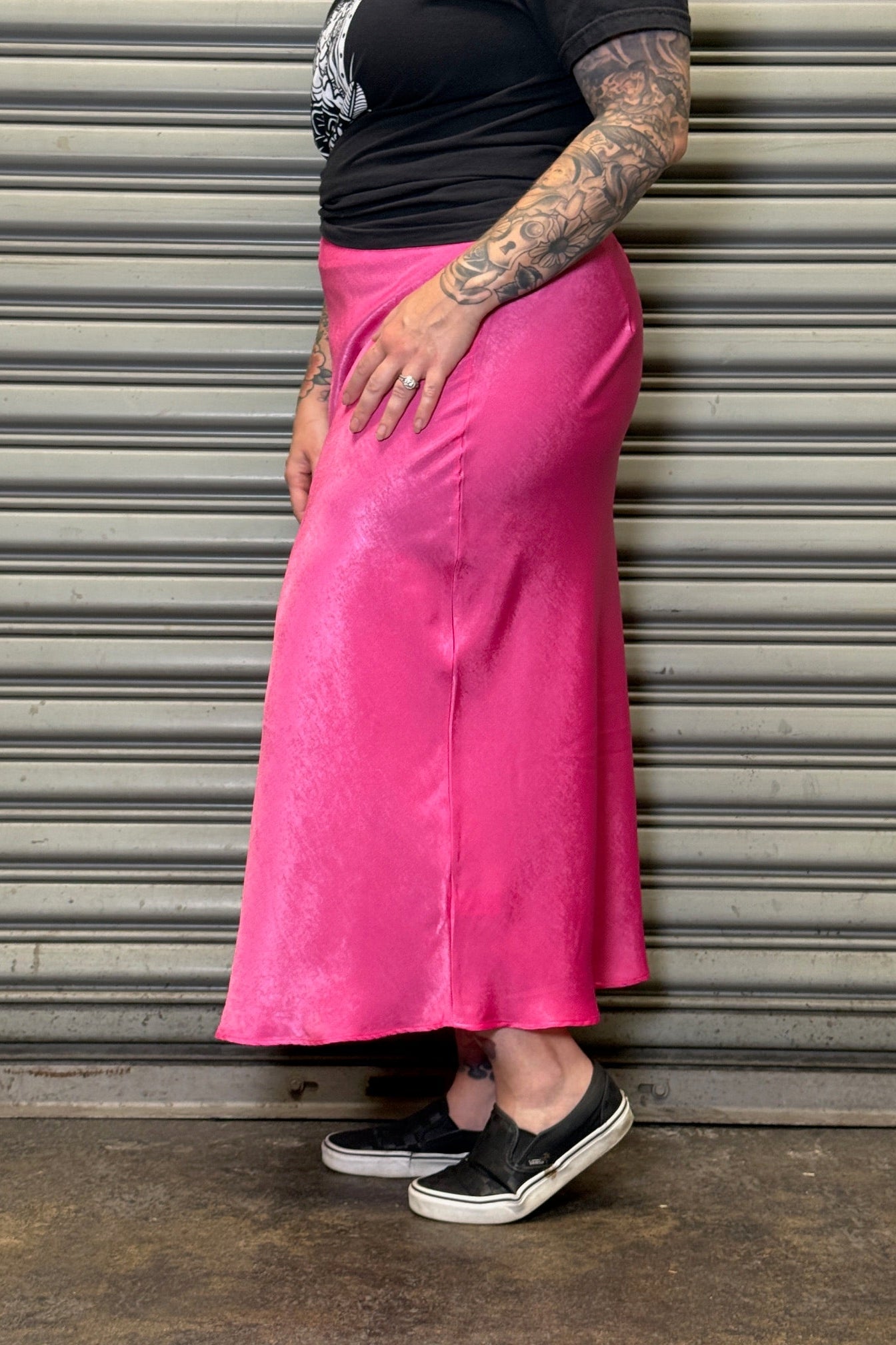 Person wearing a bright pink skirt standing against a metallic shutter.