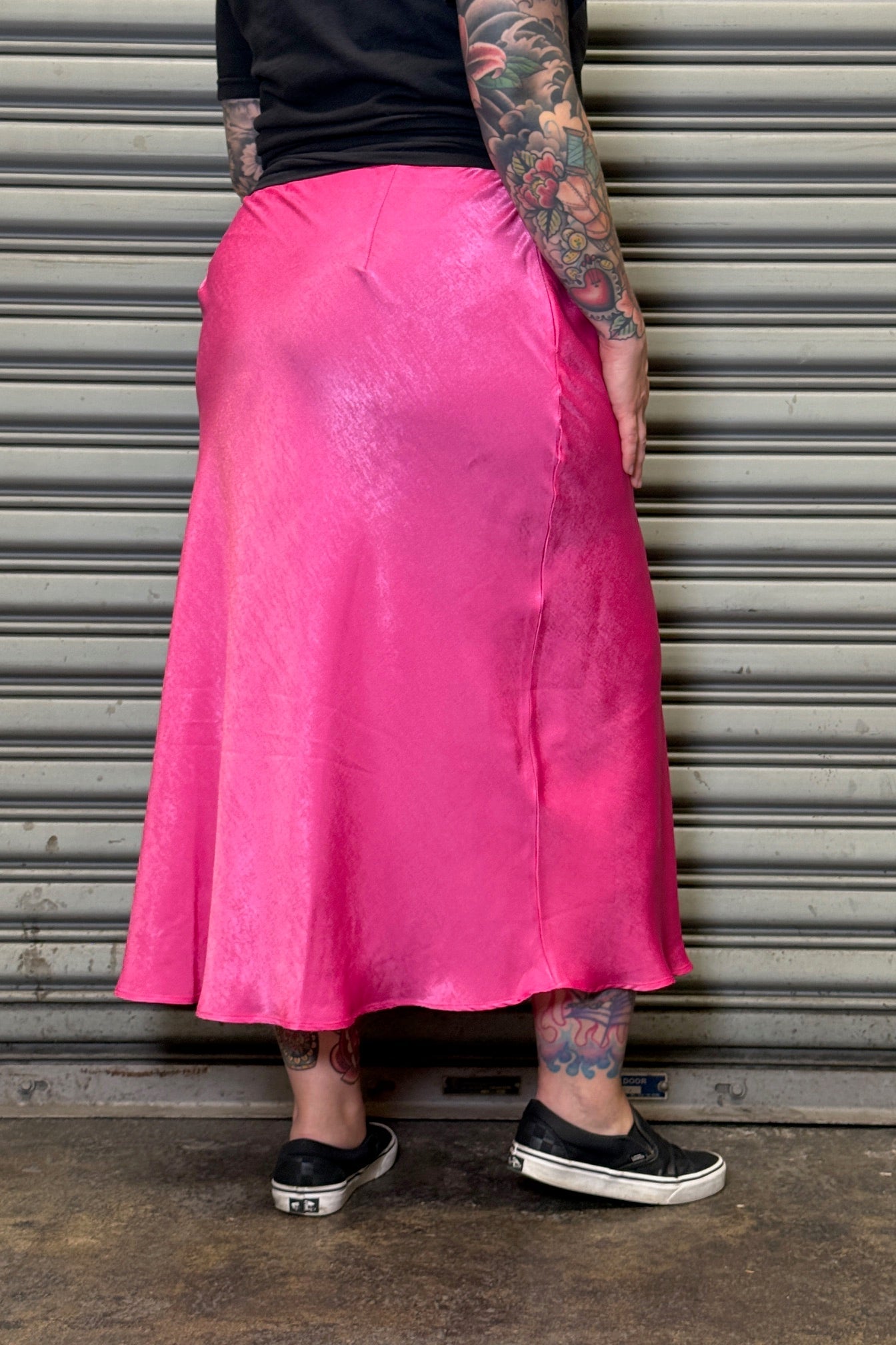Person wearing a bright pink skirt standing in front of a closed metal shutter.