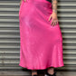 Person wearing a black t-shirt and pink skirt standing against a metal shutter.