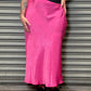 Person wearing a black t-shirt and pink skirt standing against a metallic shutter.