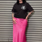Person wearing a black t-shirt and pink skirt standing in front of a metal shutter.