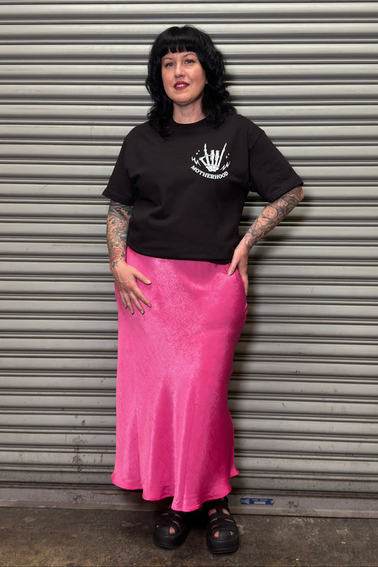 Person wearing a black t-shirt and pink skirt standing in front of a metal shutter.