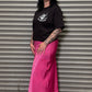 Person wearing a black t-shirt and pink skirt standing in front of a metal shutter.