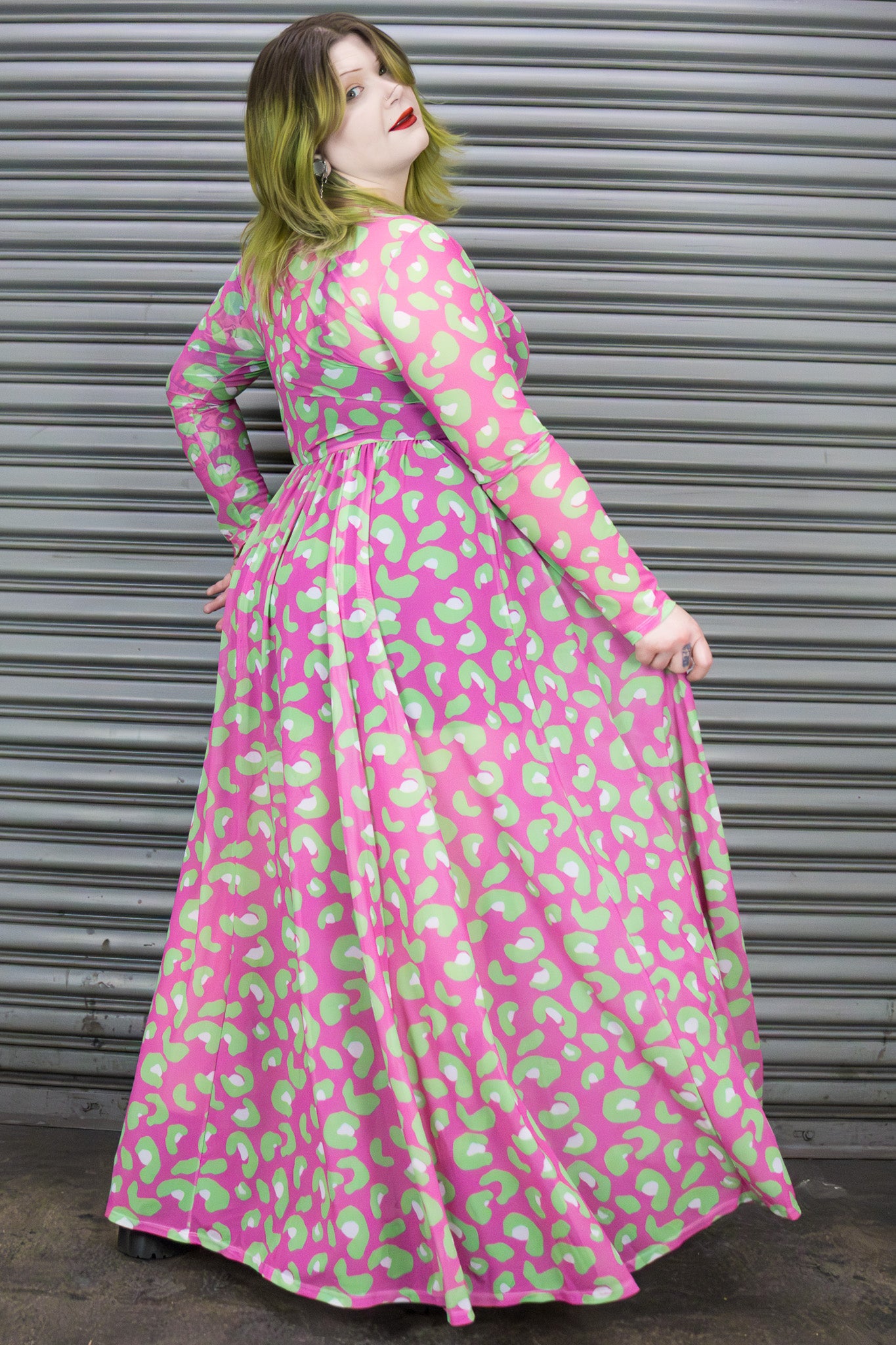 Person wearing a pink and green patterned dress standing in front of a metallic shutter.