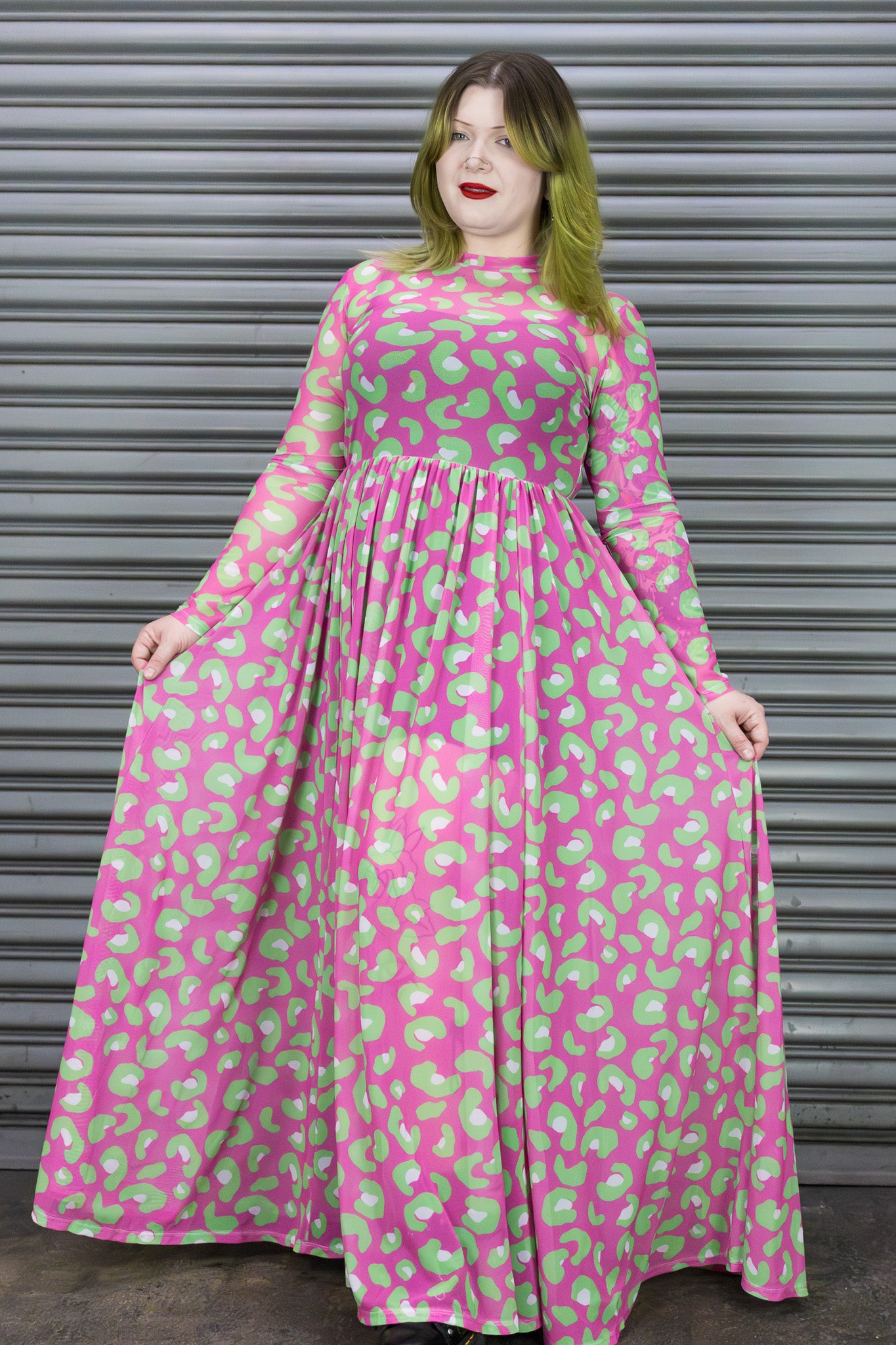 Woman wearing a pink dress with green pattern standing in front of a metallic shutter.
