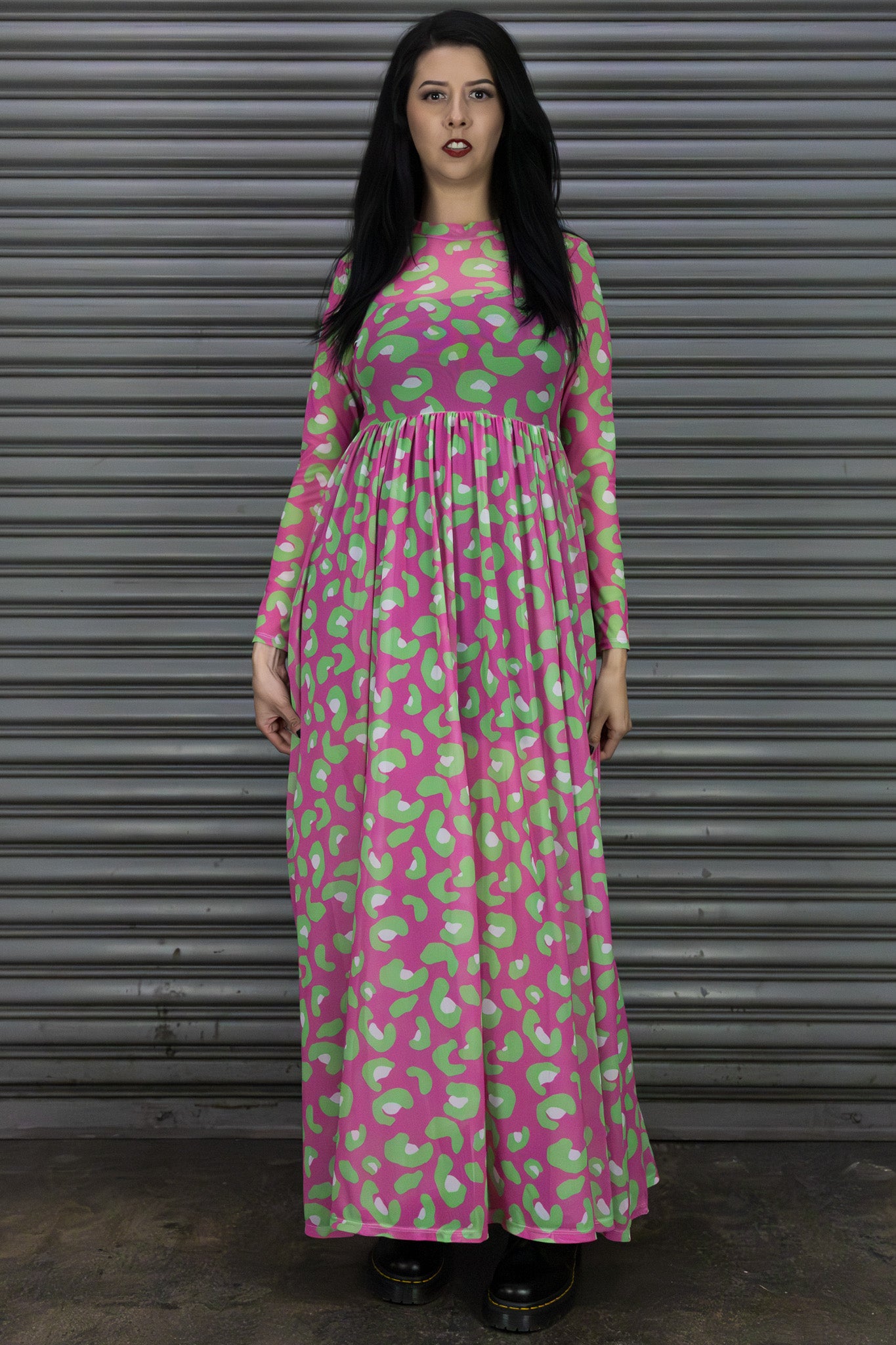 Woman wearing a pink and green patterned dress standing in front of a metallic shutter.