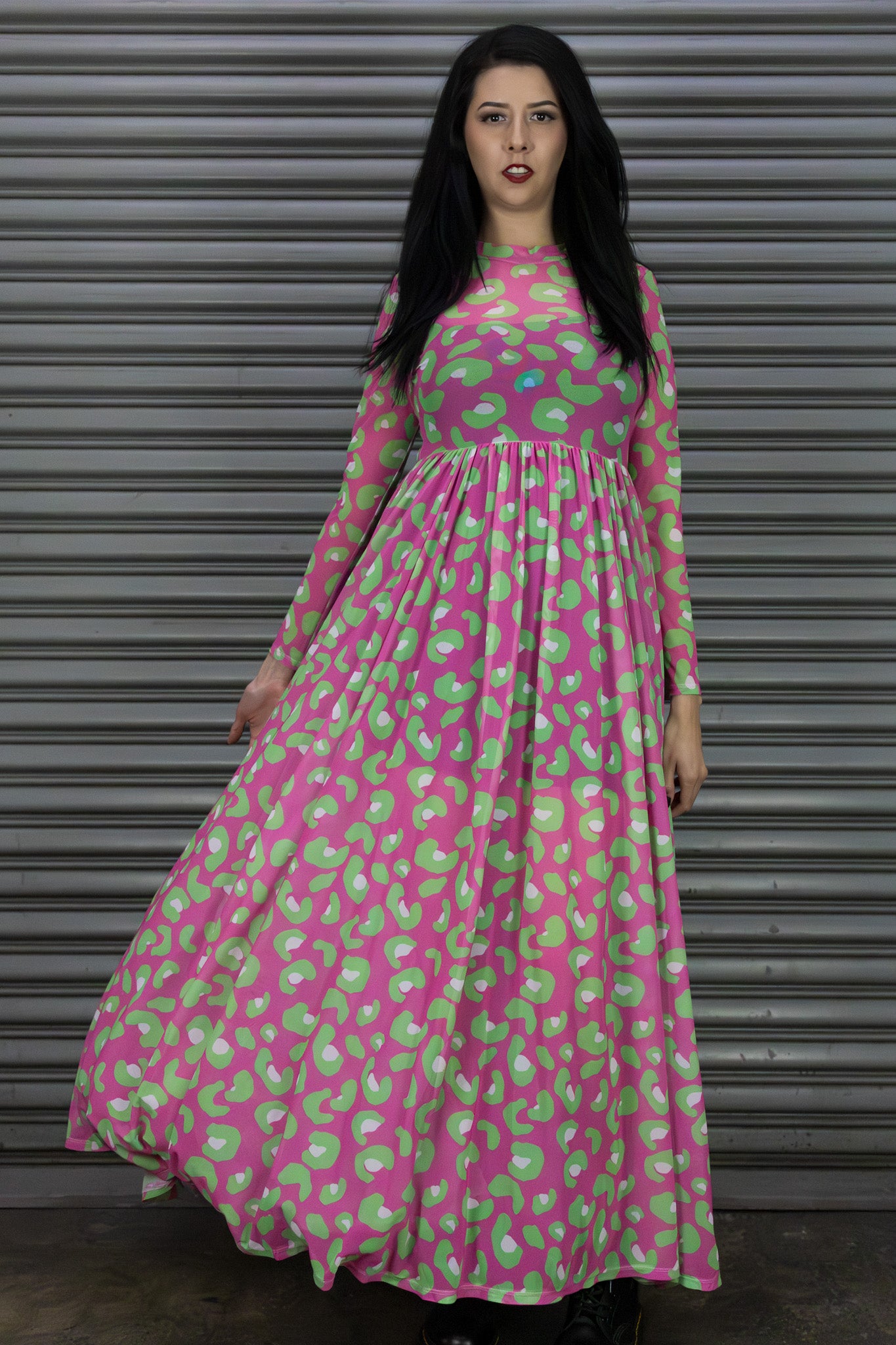 Woman wearing a pink and green patterned dress standing in front of a metallic shutter.