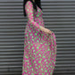 Woman wearing a pink dress with green pattern standing against a metallic shutter.