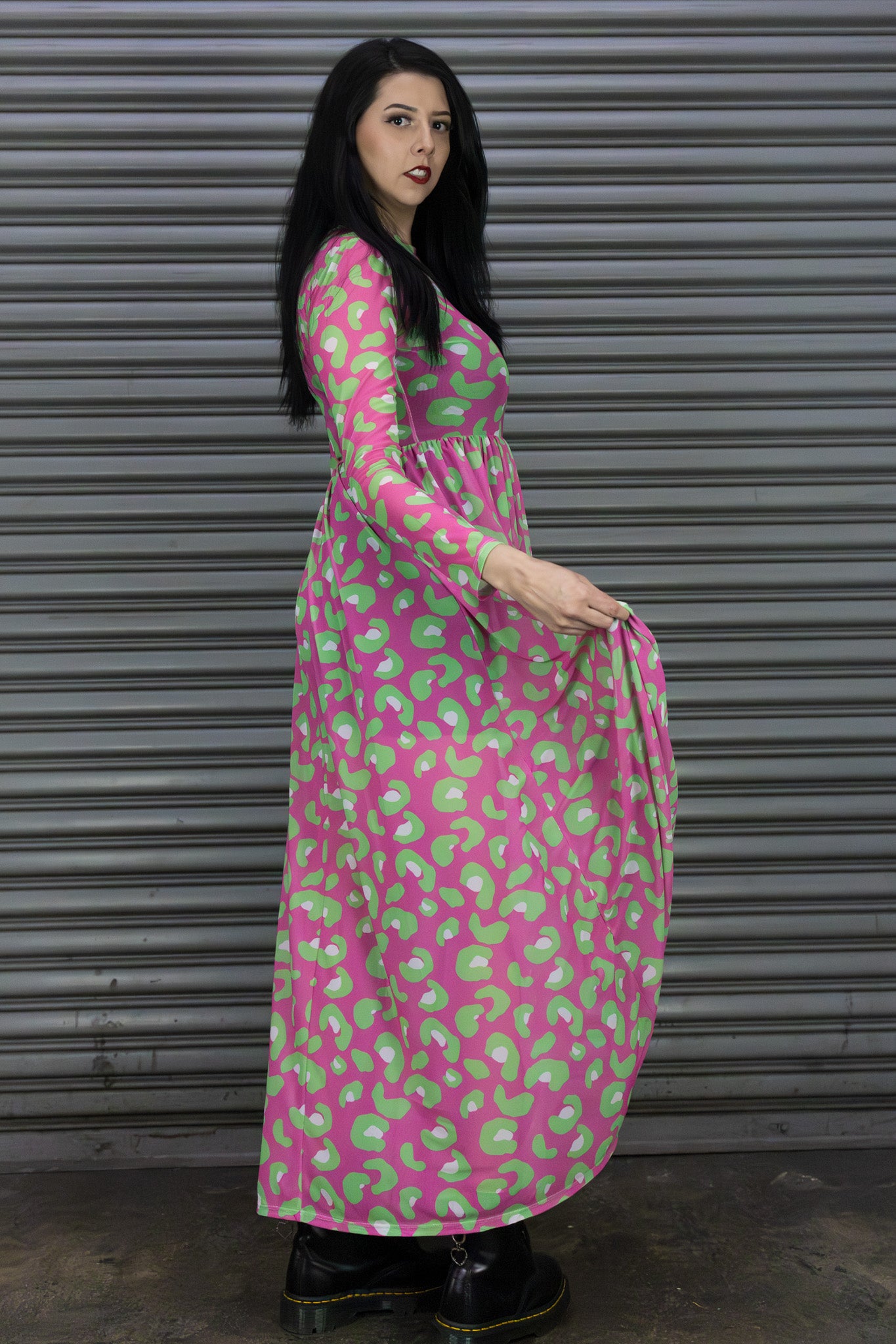 Woman wearing a pink dress with green pattern standing against a metallic shutter.