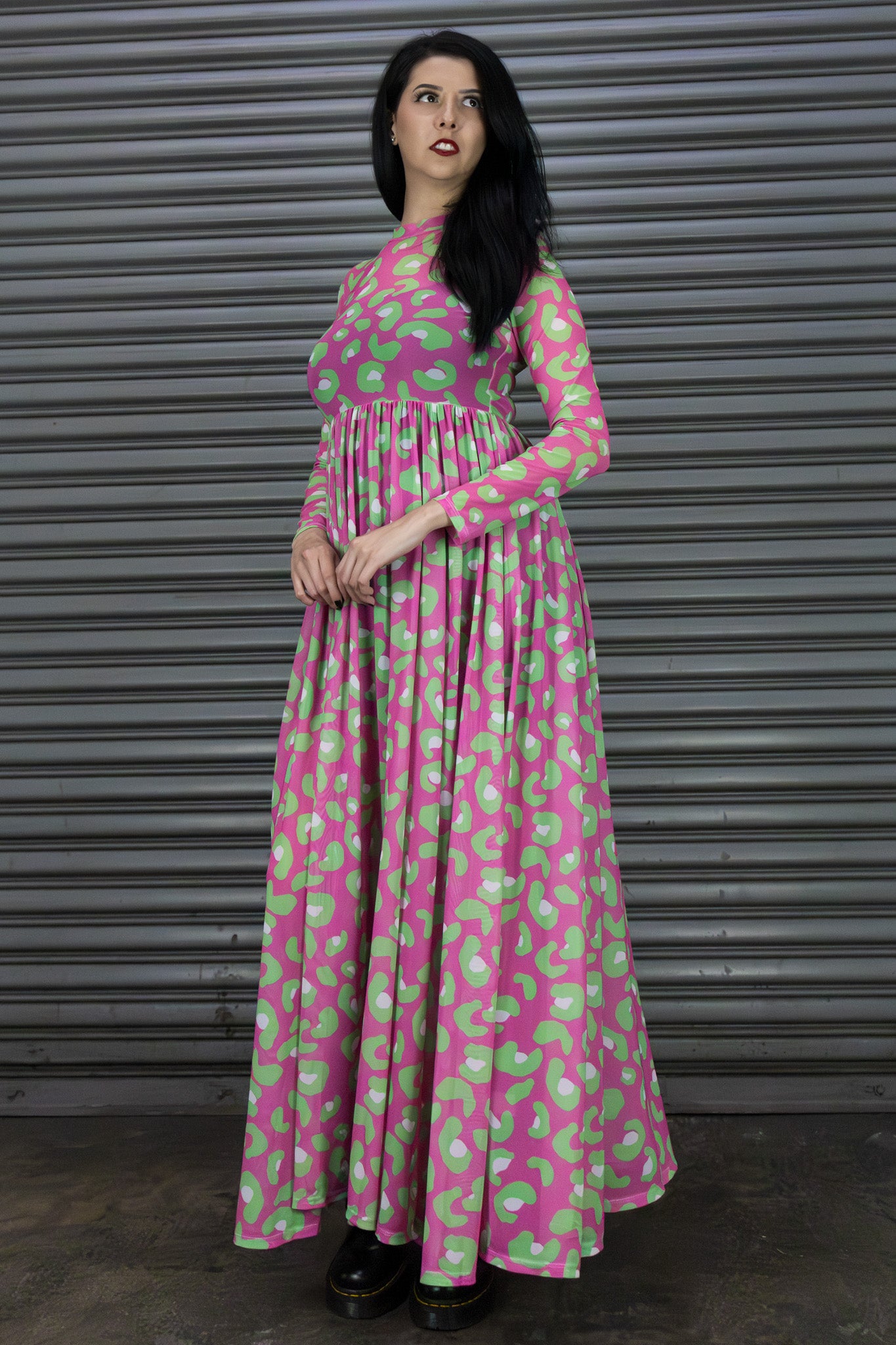 Woman wearing a pink and green patterned dress against a metallic shutter background
