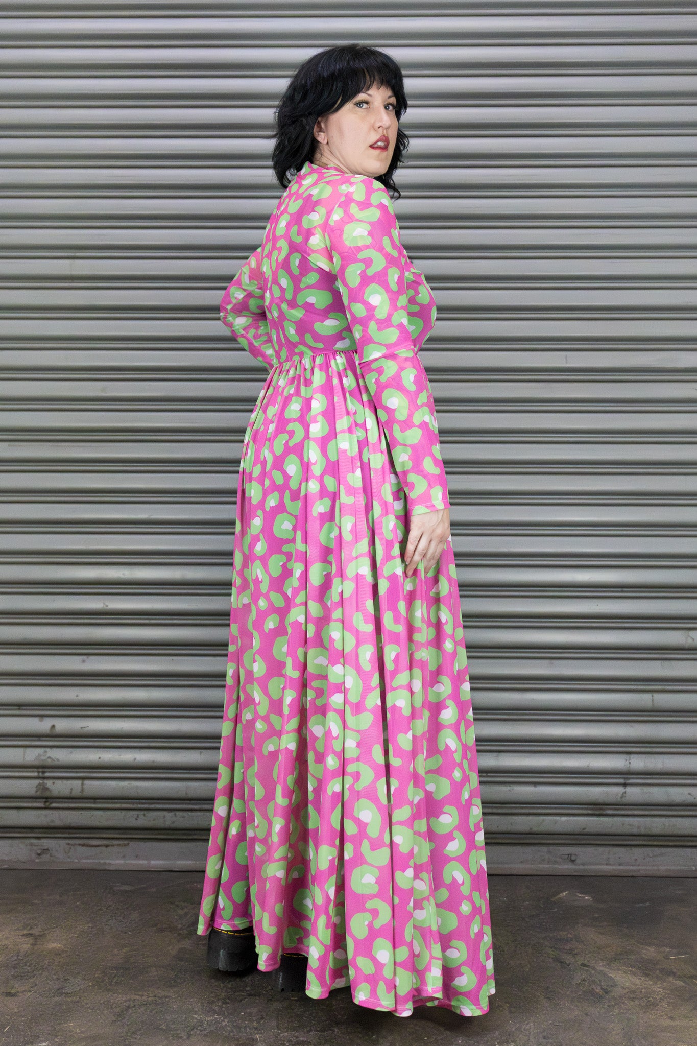 Woman wearing a pink and green patterned dress standing in front of a metallic shutter.