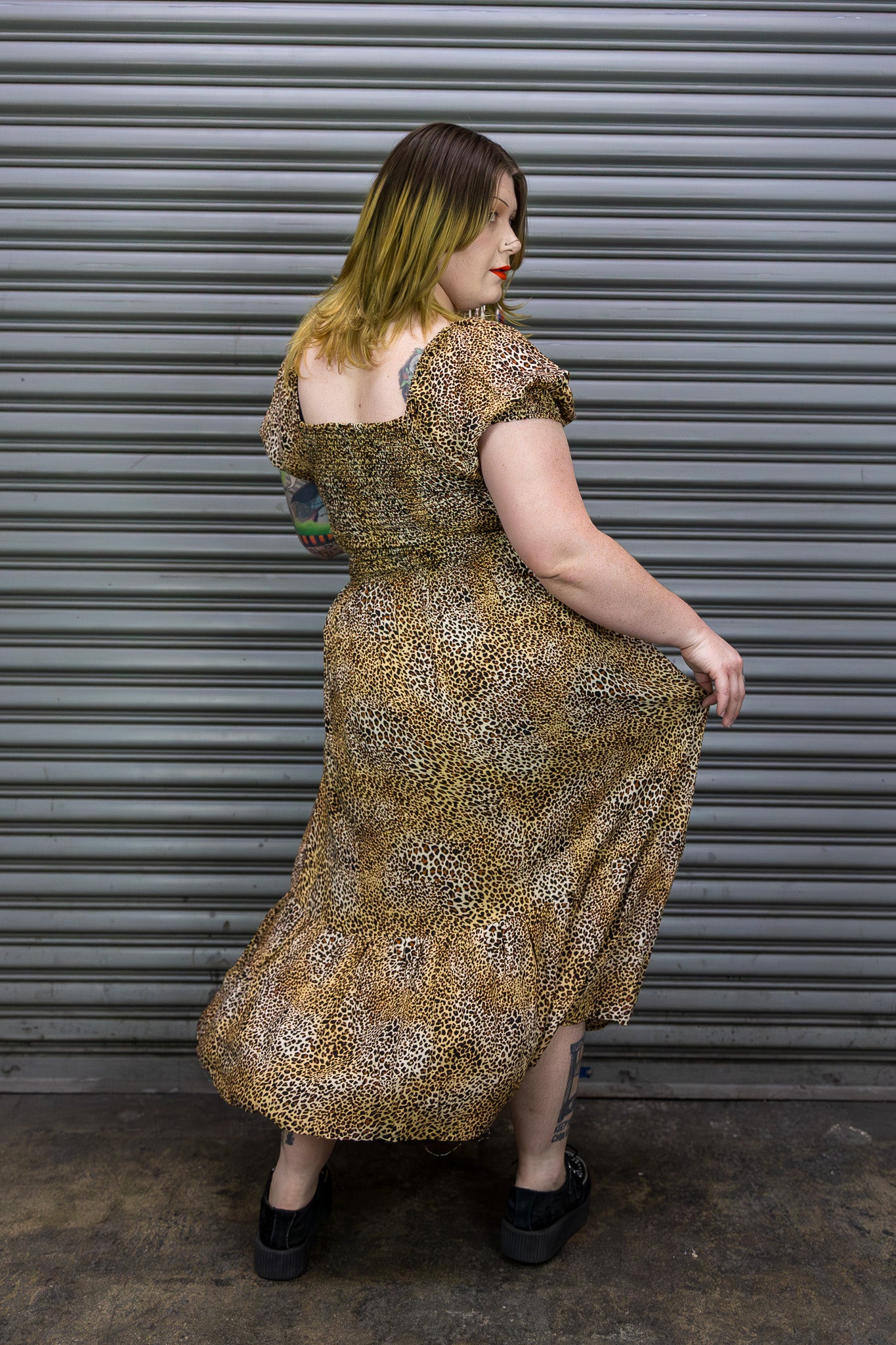 Woman in a patterned dress standing against a metal shutter.
