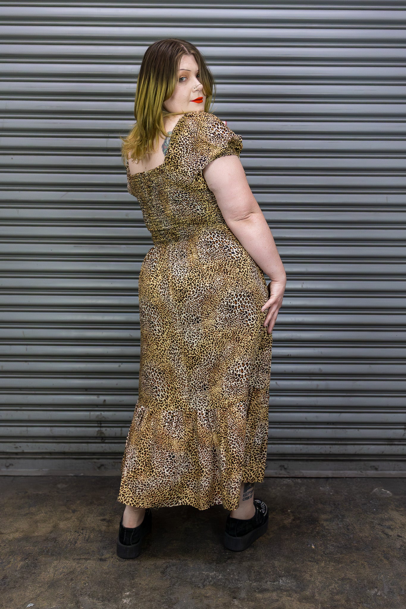 Woman wearing a patterned dress standing in front of a metal shutter.