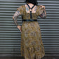 Person wearing a gold patterned dress with a black belt in front of a metal shutter.
