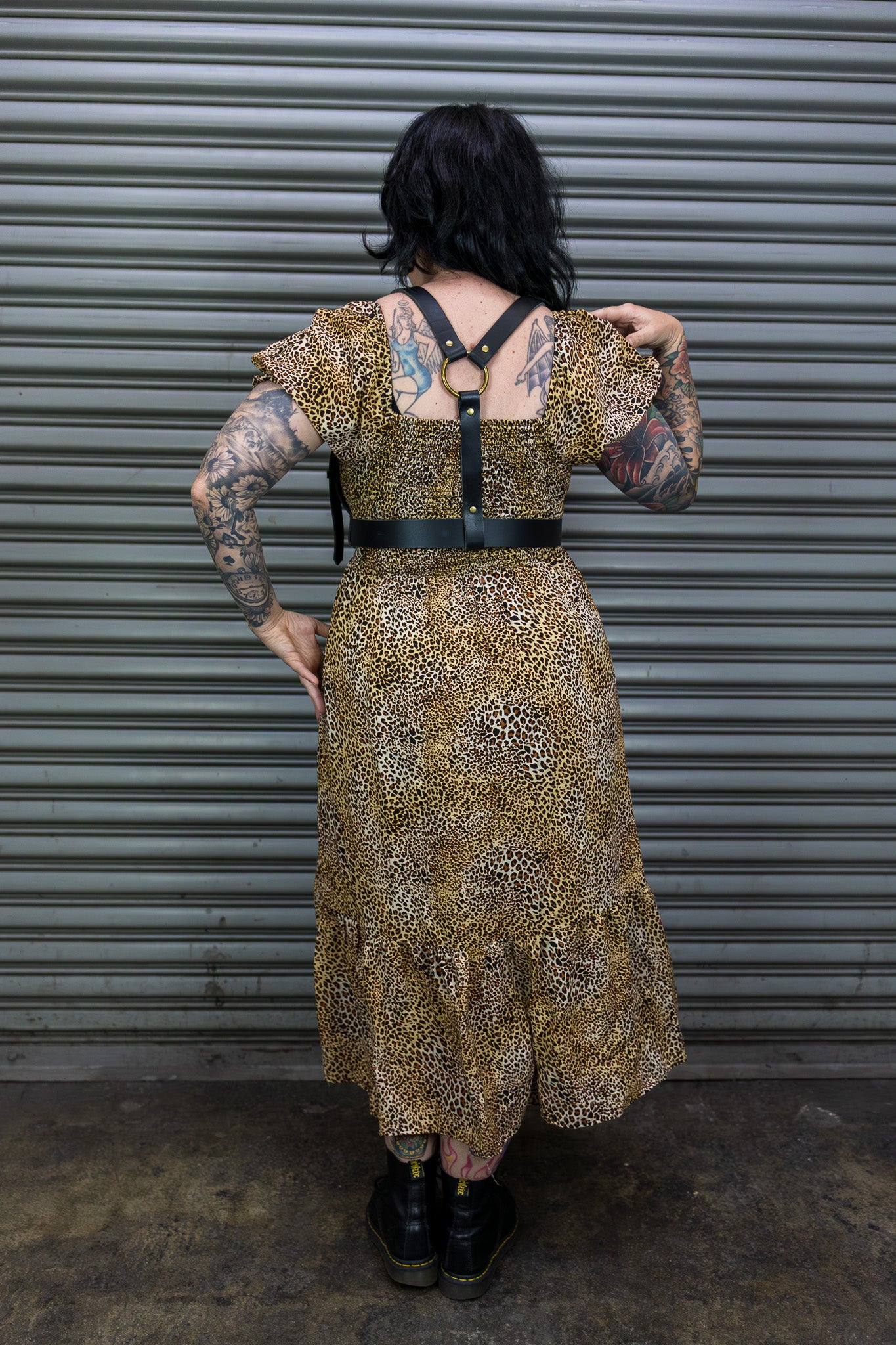 Person wearing a gold patterned dress with a black belt in front of a metal shutter.