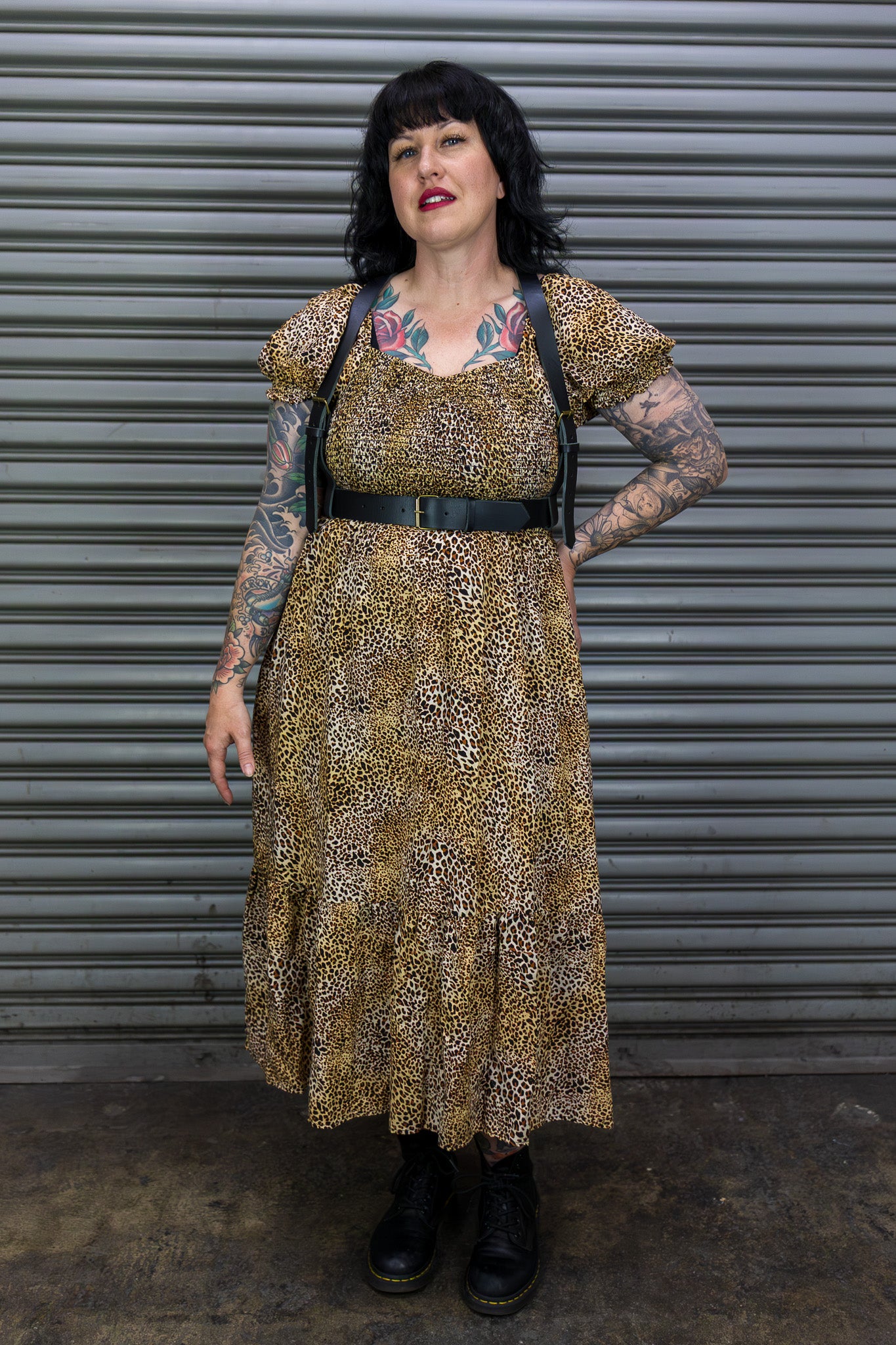 Woman wearing a patterned dress with tattoos standing in front of a metallic shutter.