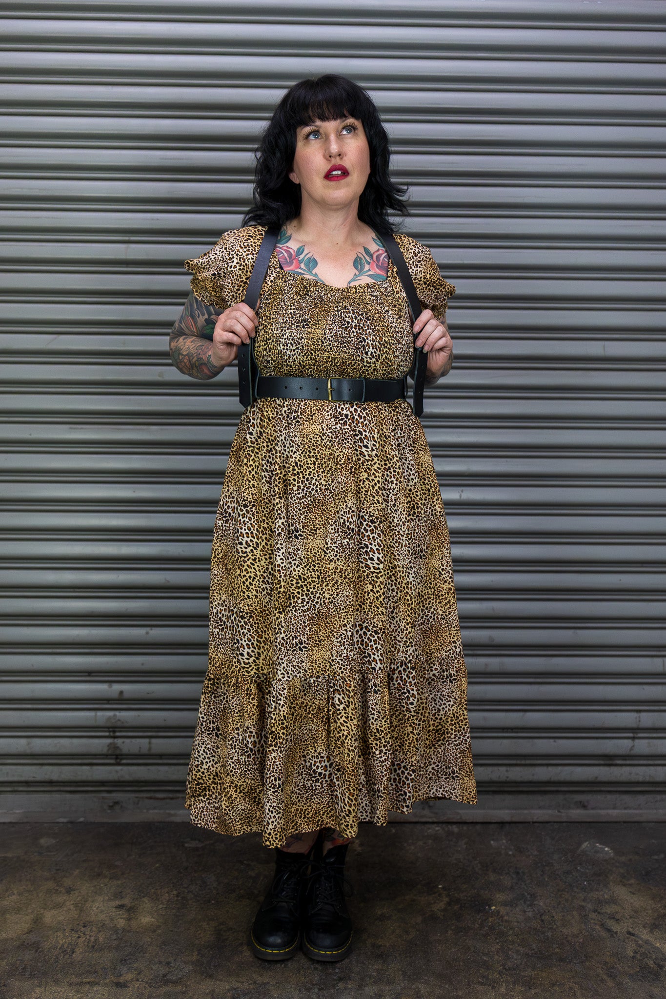 Woman wearing a leopard print dress with tattoos standing in front of a metal shutter.