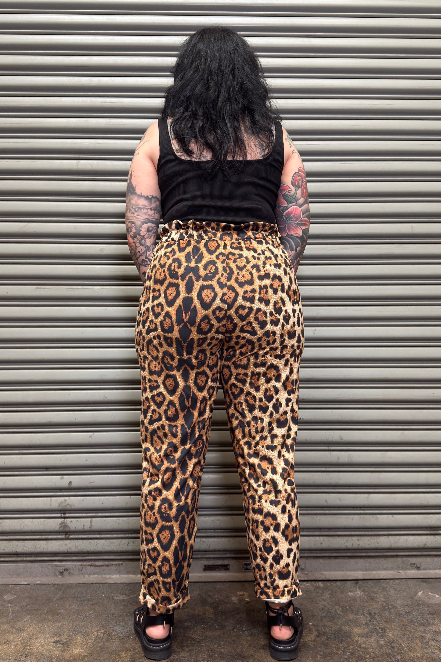 Person wearing leopard print pants standing in front of a metal shutter.