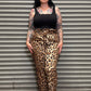 Person wearing leopard print pants and black tank top standing against a metal shutter.