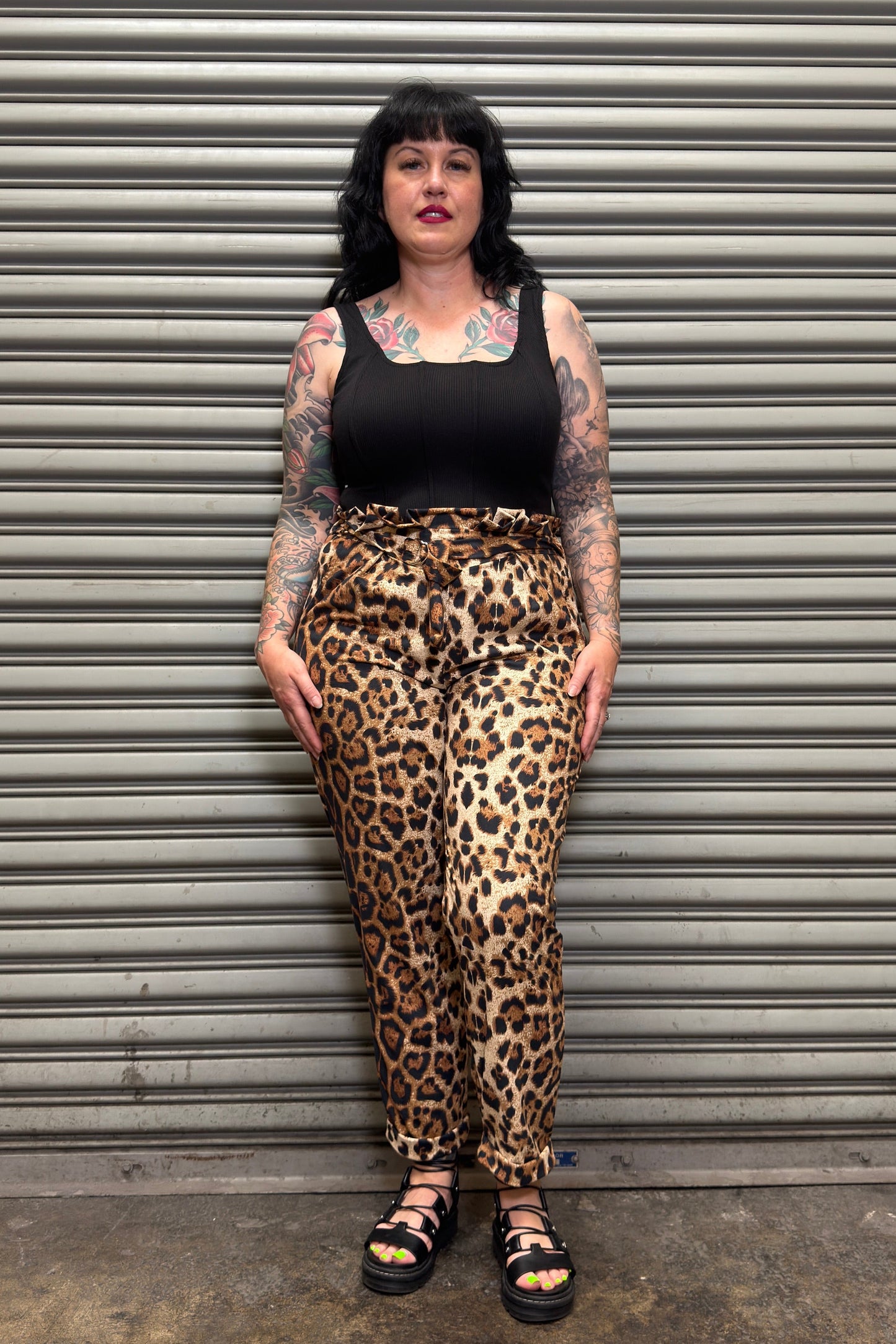 Person wearing leopard print pants and black tank top standing against a metal shutter.
