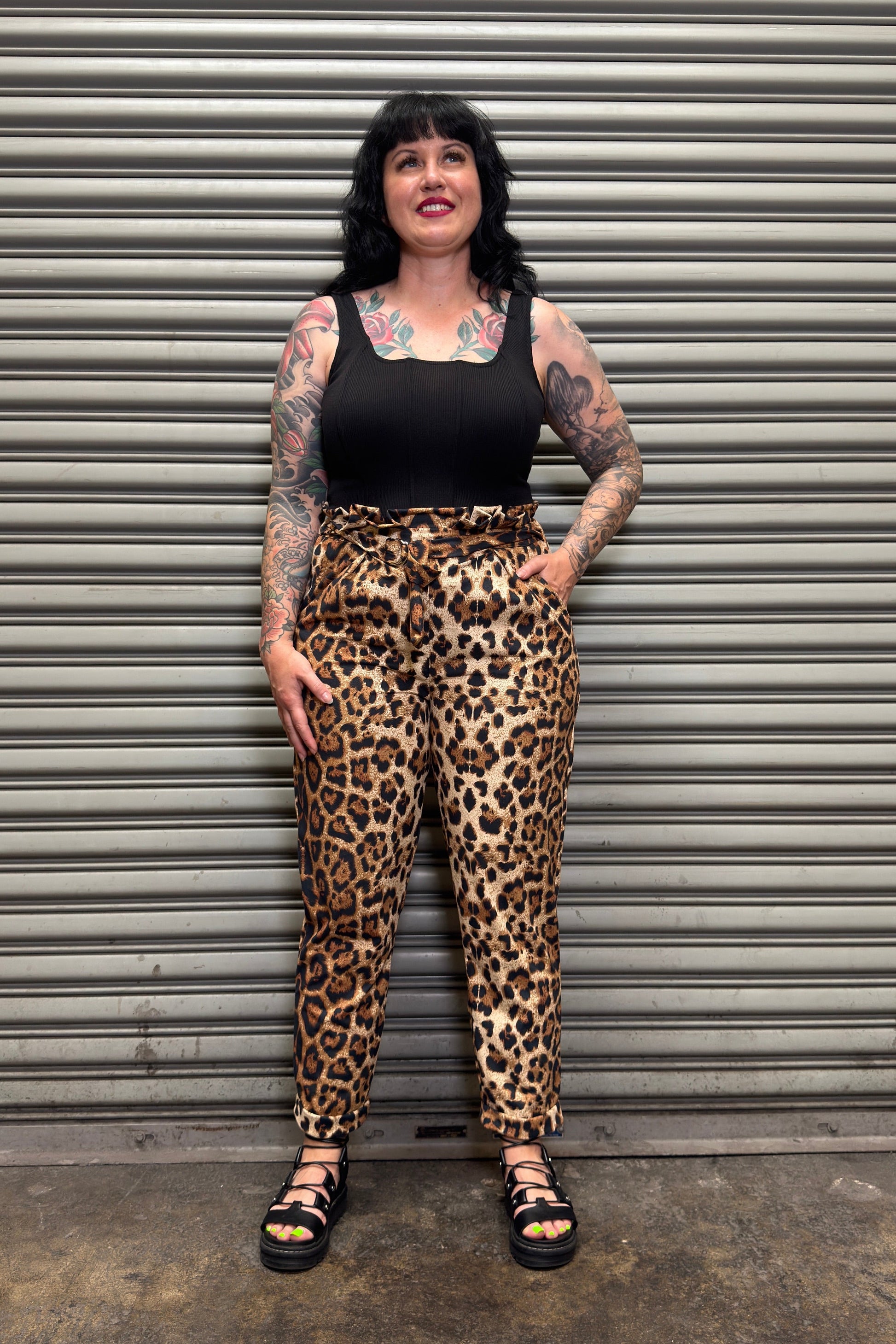 Person wearing leopard print pants and a black top standing in front of a metal shutter.