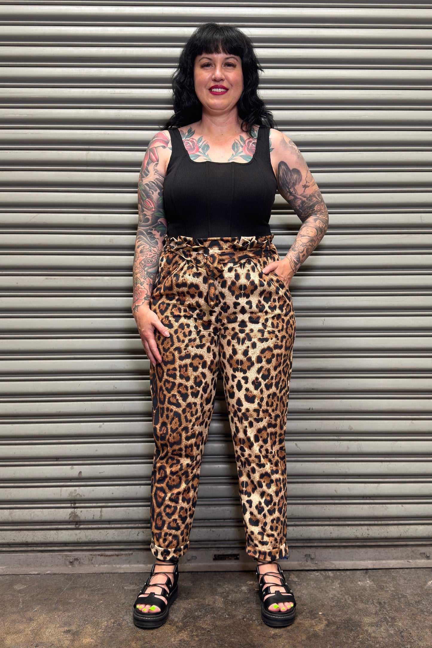 Person wearing leopard print pants and a black top standing in front of a metal shutter.