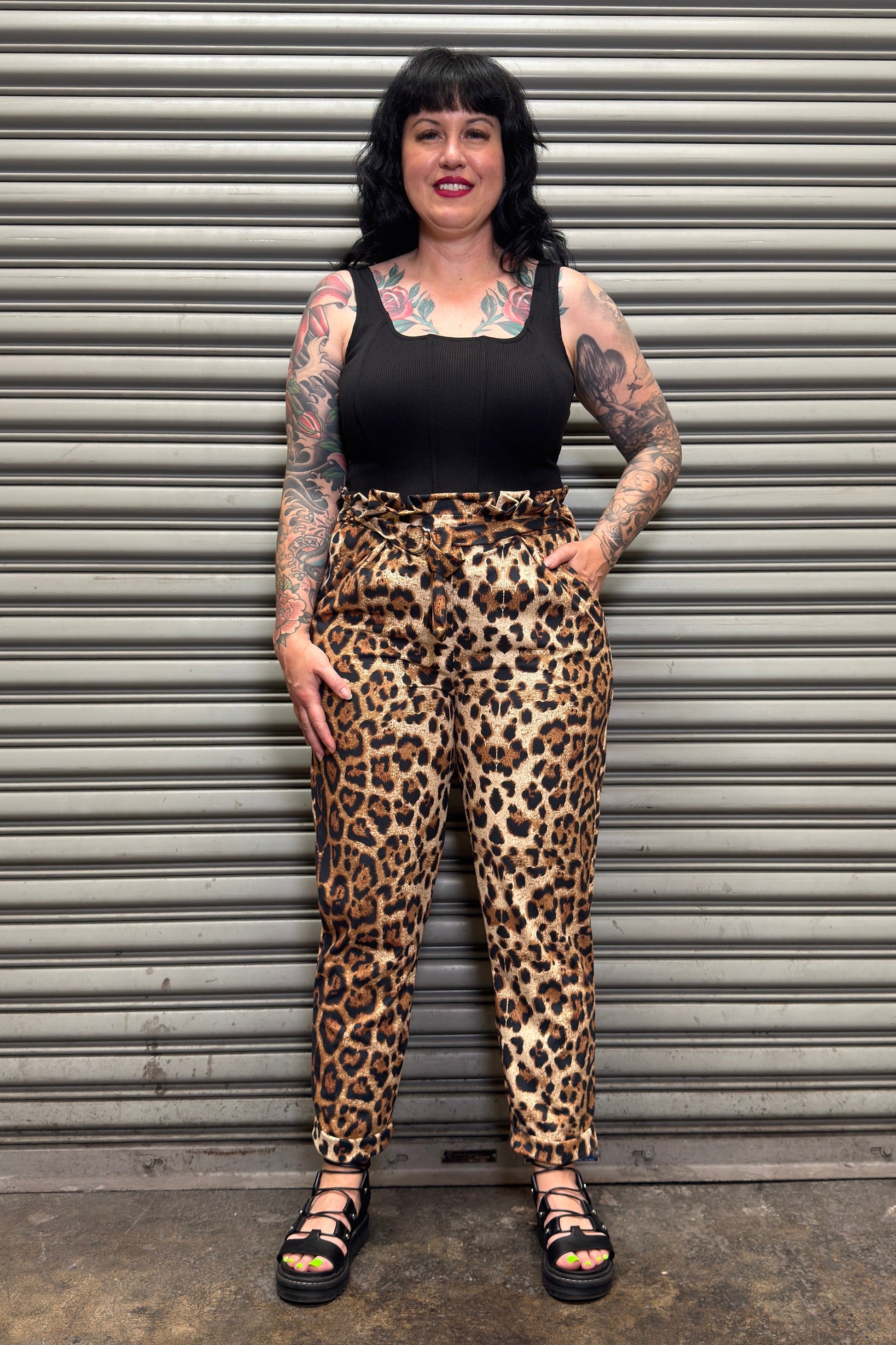 Person wearing leopard print pants and a black top standing in front of a metal shutter.