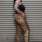 Person wearing leopard print pants and black top standing against a metal shutter.