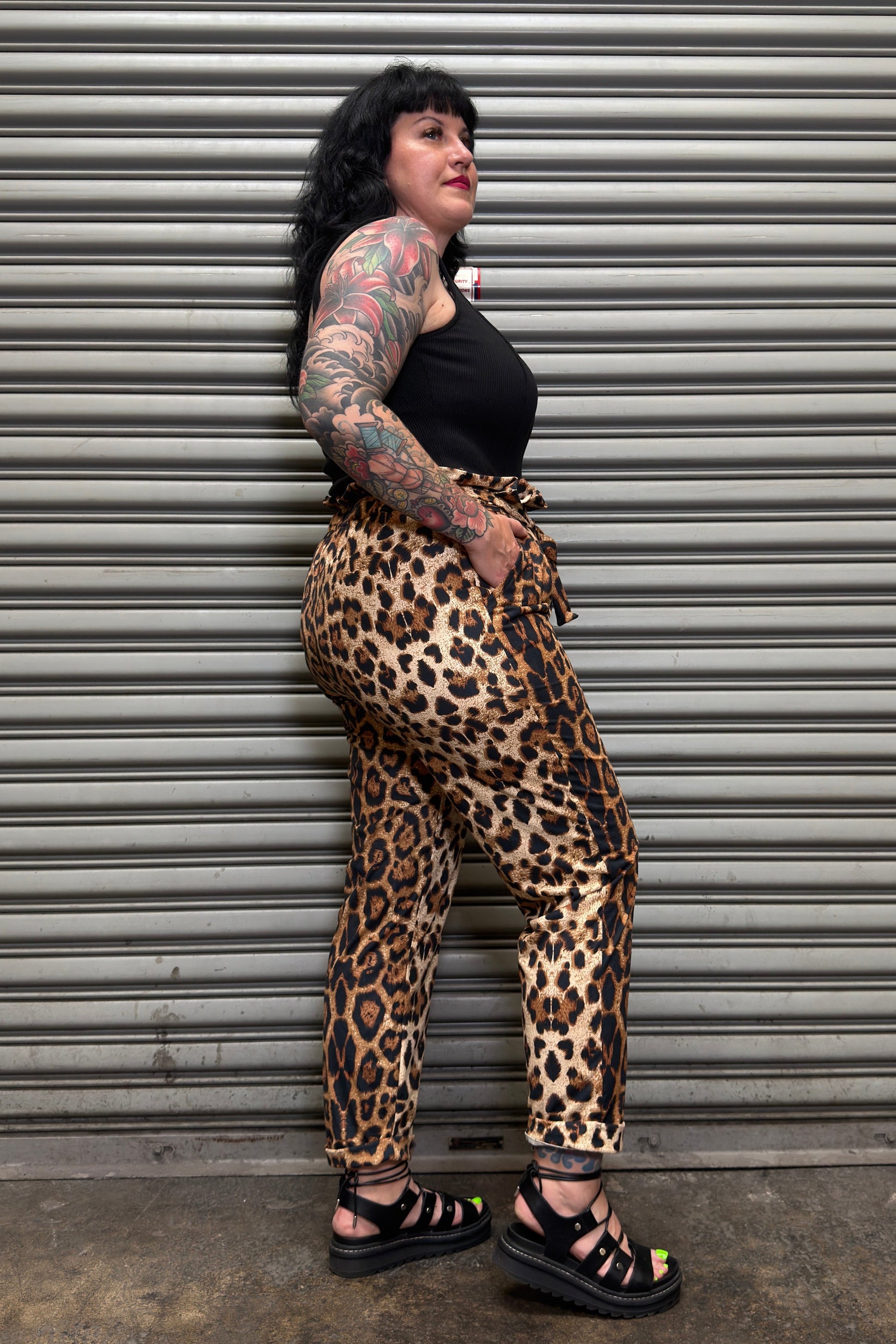 Person wearing leopard print pants and black top standing against a metal shutter.
