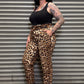 Person wearing leopard print pants and black top standing against a metal shutter.