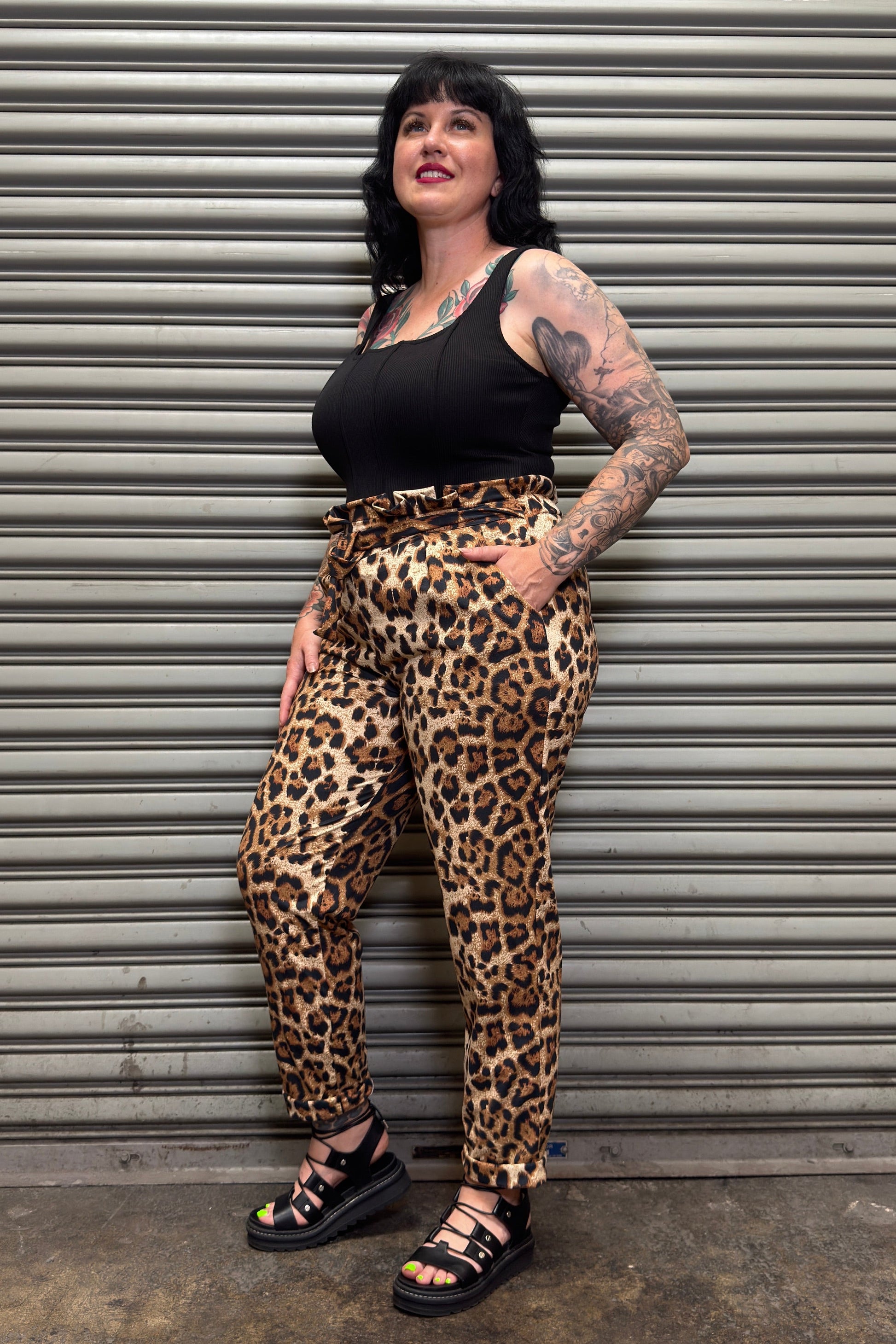 Person wearing leopard print pants and black top standing against a metal shutter.