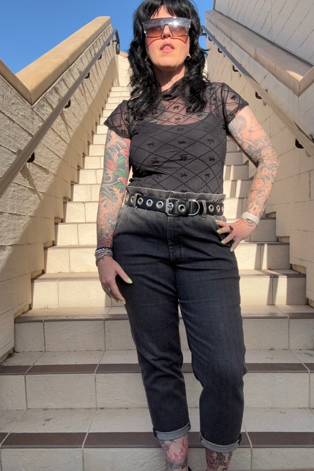 Person with tattoos standing on a staircase with a clear blue sky in the background
